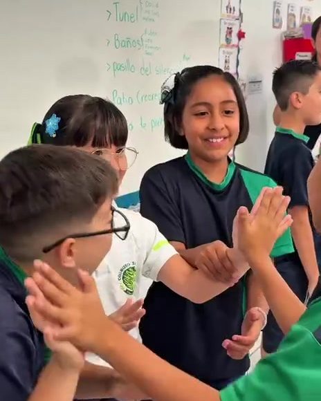 Alumnos de primaria chocando las manos y riendo en el salón el primer día de clases