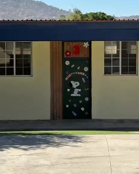 Edificio de salones de Colegio Encinos con puerta decorada y cerros de Tecate al fondo