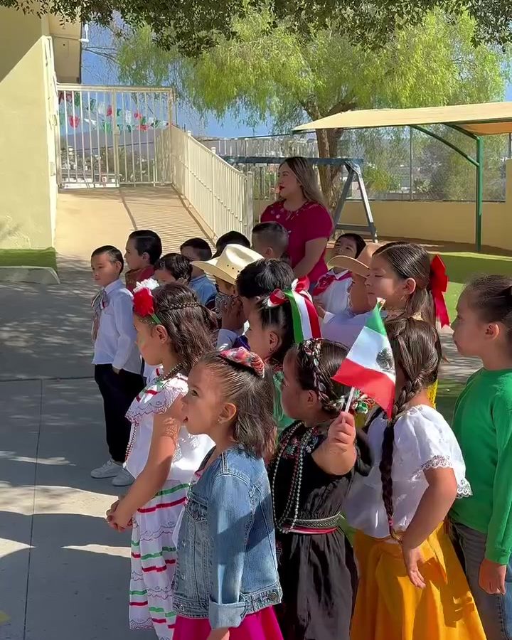 Niñas y niños de preescolar con trajes típicos mexicanos y banderitas en el patio de Colegio Encinos