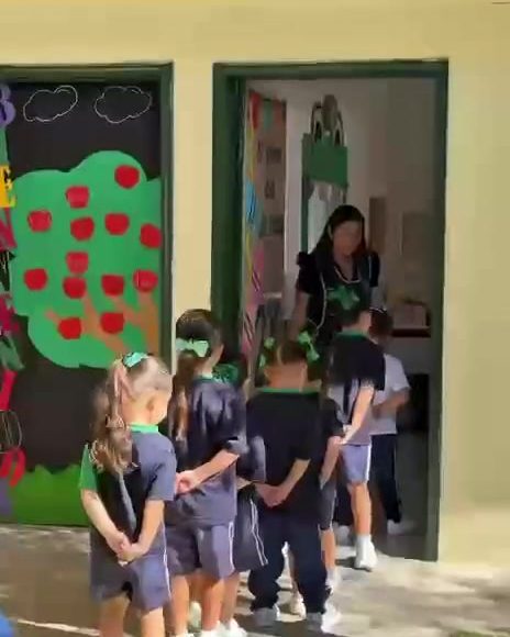 Alumnos de preescolar formados en fila para entrar a su salón decorado con un árbol de manzanas