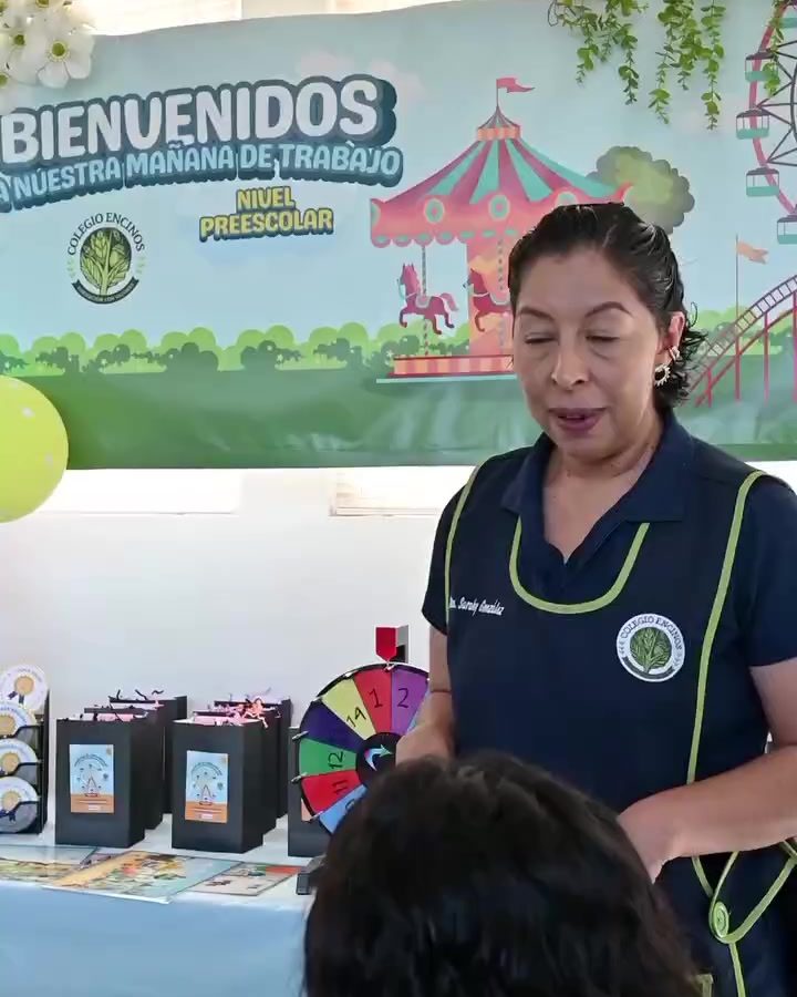 Maestra de Colegio Encinos recibiendo a los alumnos frente al letrero de bienvenida del salón