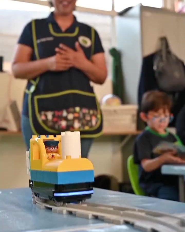 Maestra de preescolar con mandil de colores platicando con su grupo dentro del salón