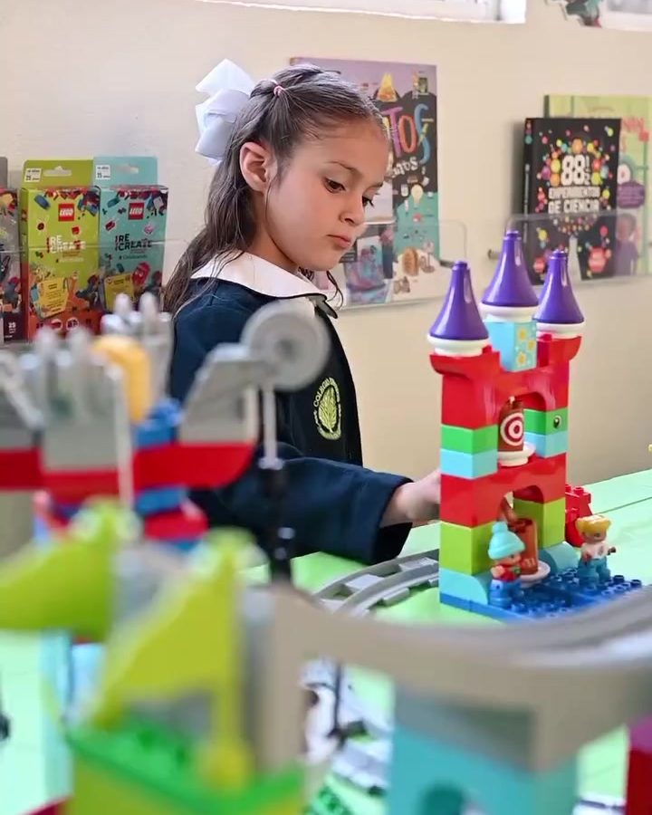 Niña de preescolar con moño blanco concentrada en un castillo de bloques con torres moradas