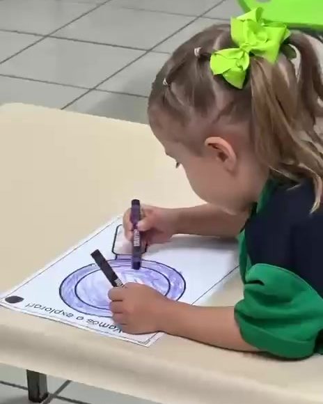 Niña de maternal con moño verde coloreando un círculo en su hoja