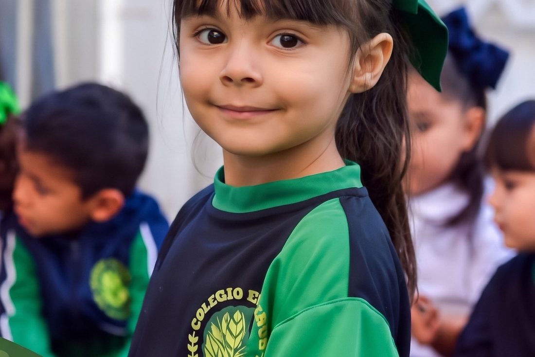 Niña de preescolar con chamarra verde del uniforme de Colegio Encinos sentada con su grupo en el patio