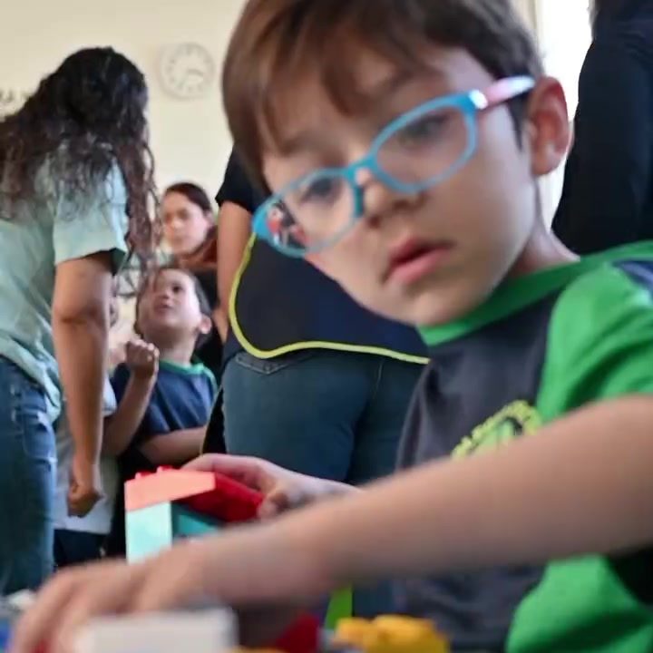 Niño de preescolar con lentes azules armando una construcción de bloques de colores en su mesa