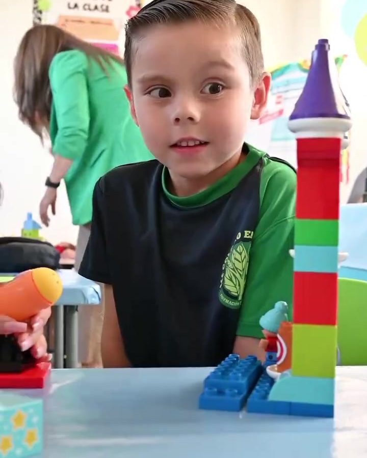 Niño de preescolar sonriendo junto a la torre de bloques de colores que construyó