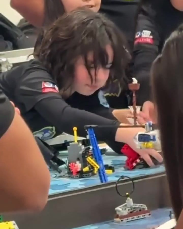 Alumna de primaria ajustando las piezas de su robot LEGO en el tablero de competencia